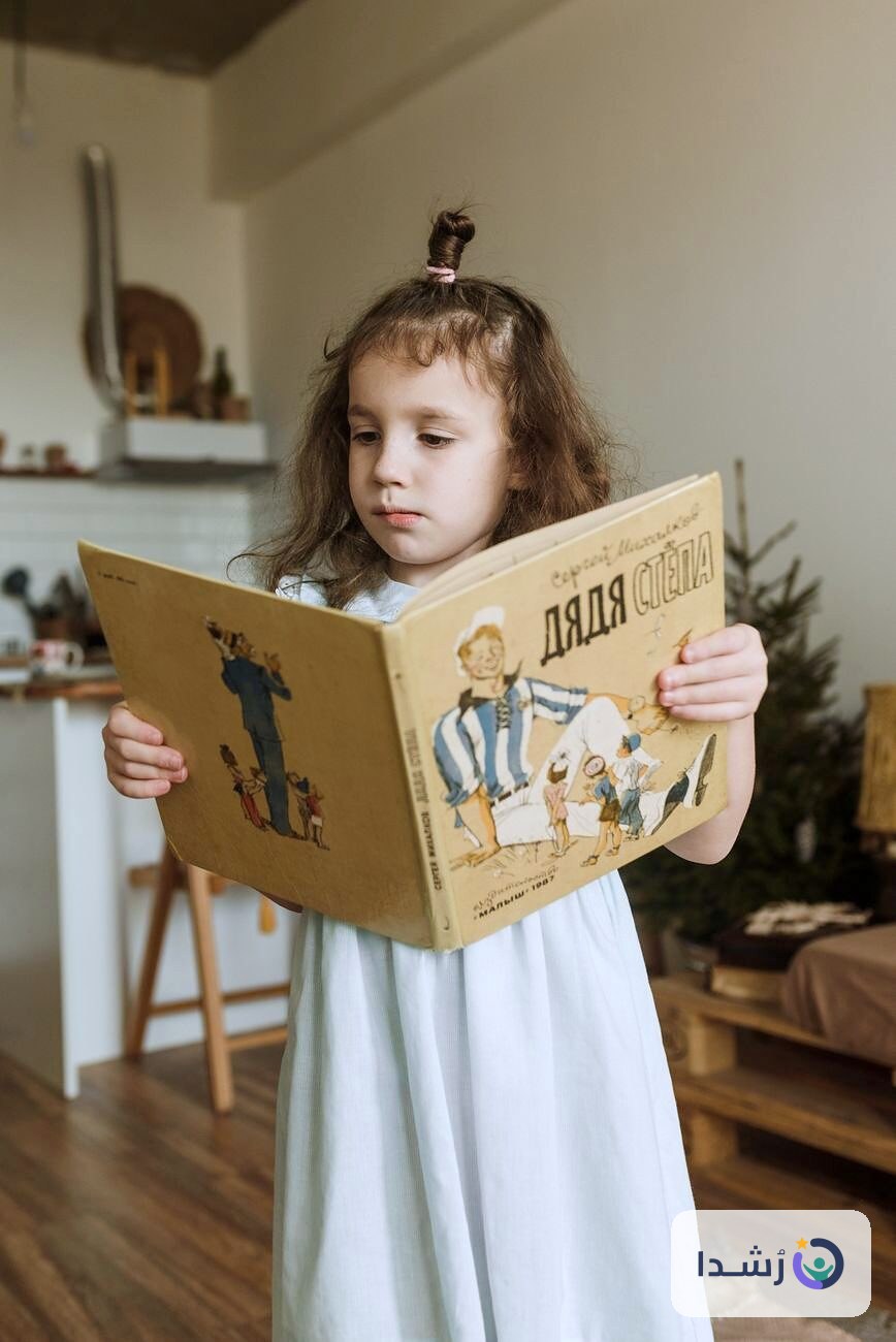 طفلة صغيرة تقرأ كتابًا في غرفة مريحة.