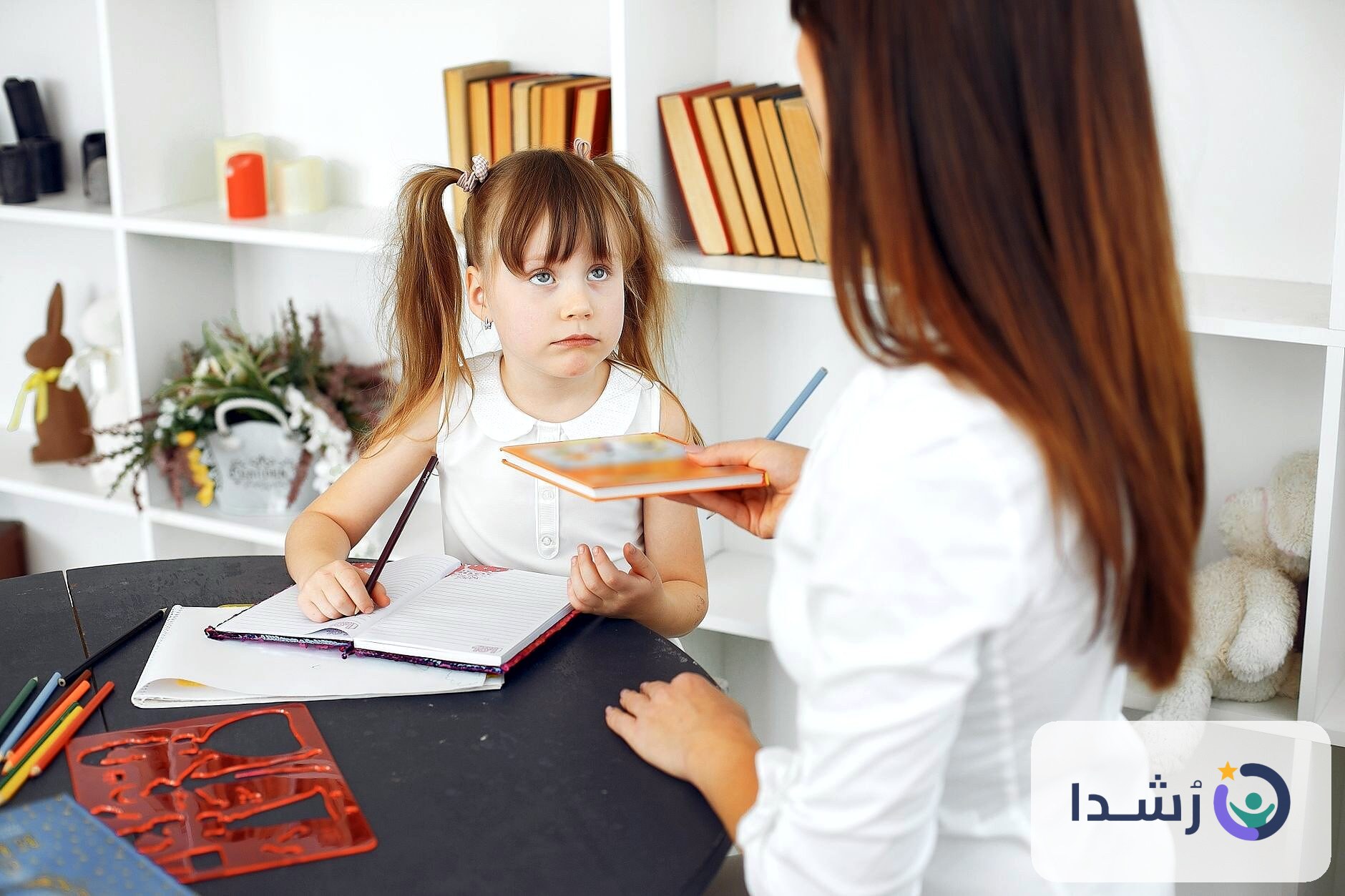 طفلة تتعلم مع معلمتها في بيئة تعليمية مريحة.