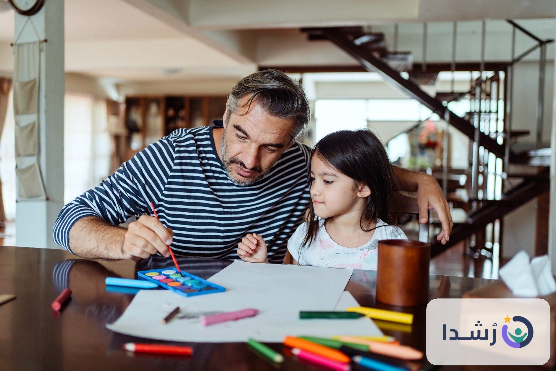 أب يعلم ابنته الرسم باستخدام الألوان في المنزل