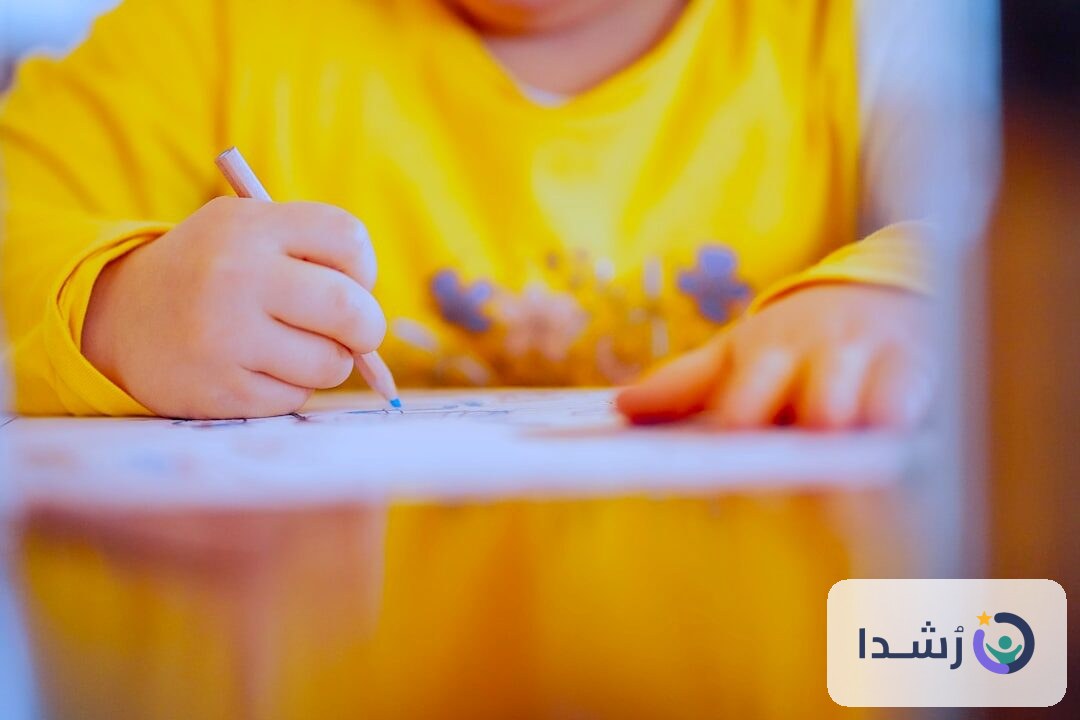 طفل صغير يرتدي قميص أصفر ويكتب باستخدام قلم ملون.