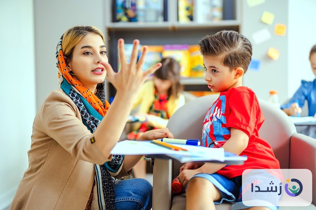 معلمة تتحدث مع طفل في فصل دراسي لتعليم اللغة العربية.