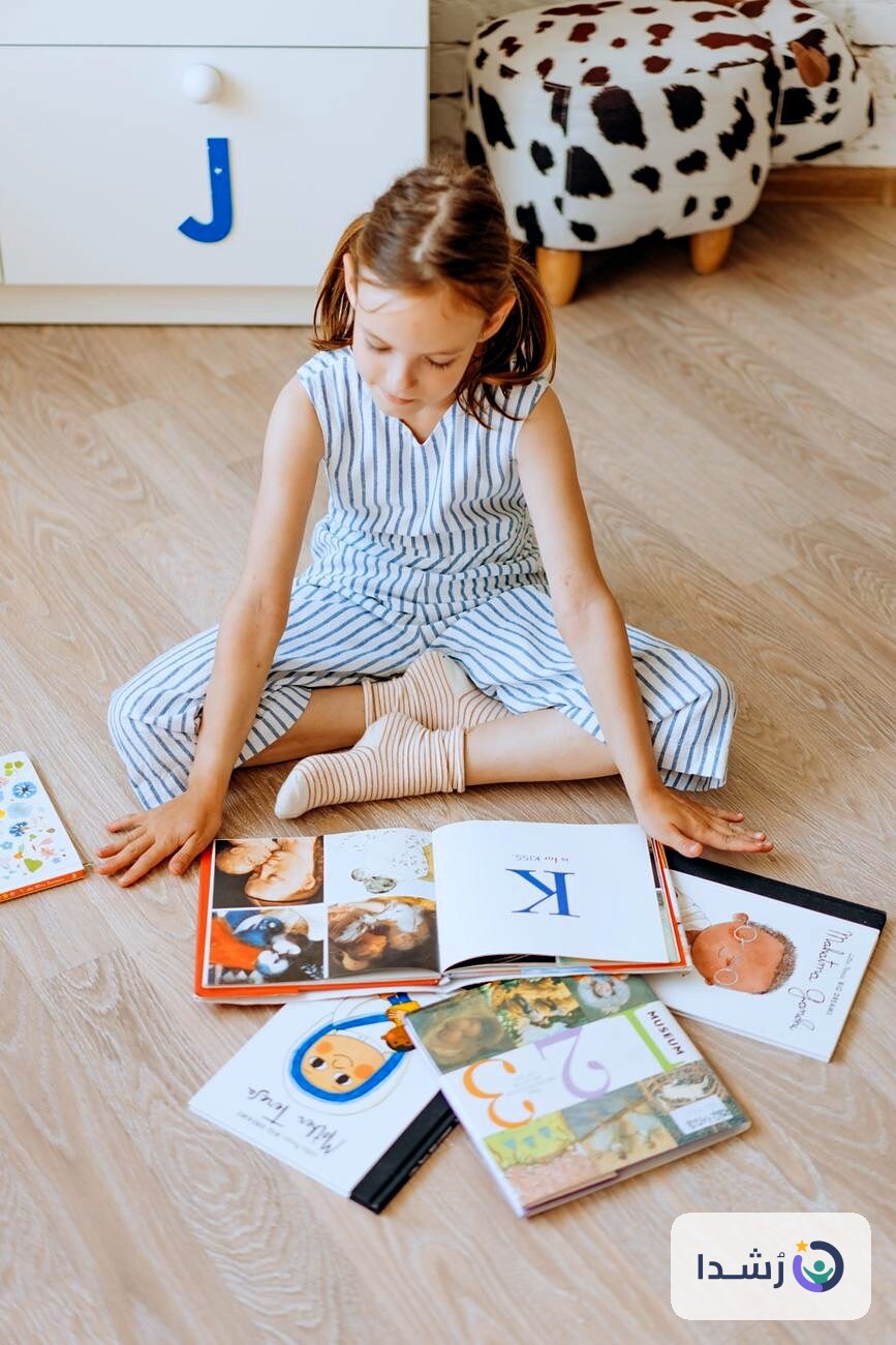 طفلة تجلس على الأرض محاطة بكتب تعليمية ملونة.