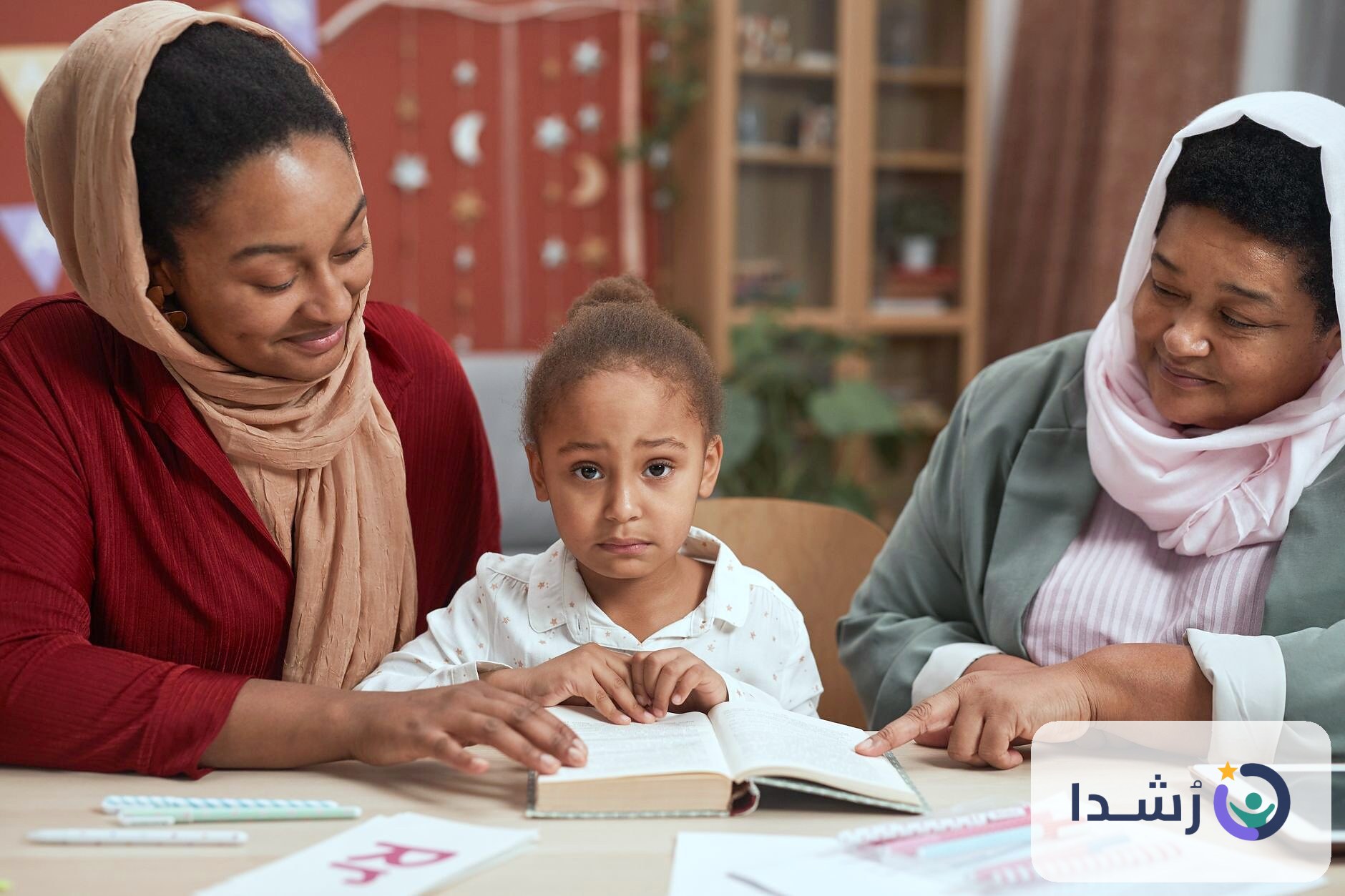 طفلة تتعلم القراءة مع والدتها وجدتها في جو عائلي دافئ.