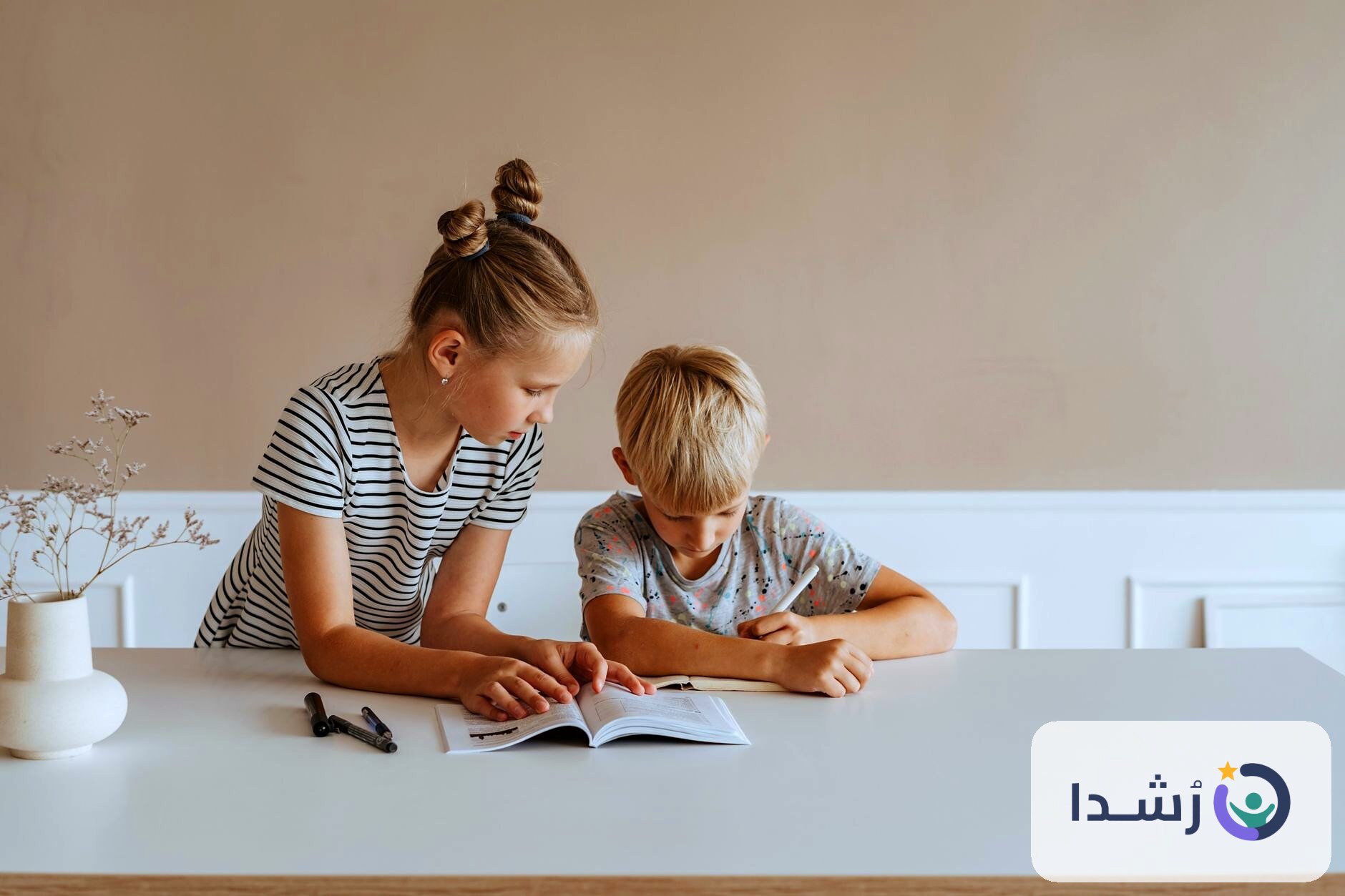 طفلان يتعلمان معًا في المنزل باستخدام كتاب وأدوات تعليمية.
