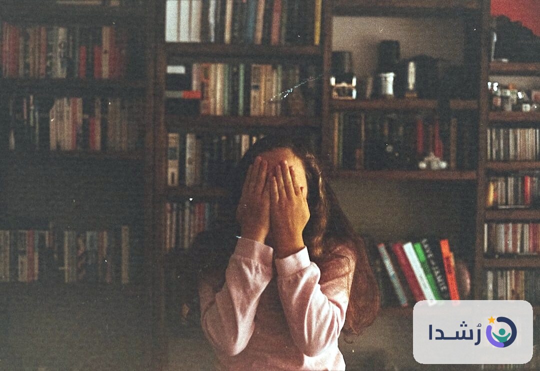 طفلة تغطي وجهها بيديها في غرفة مليئة بالكتب.