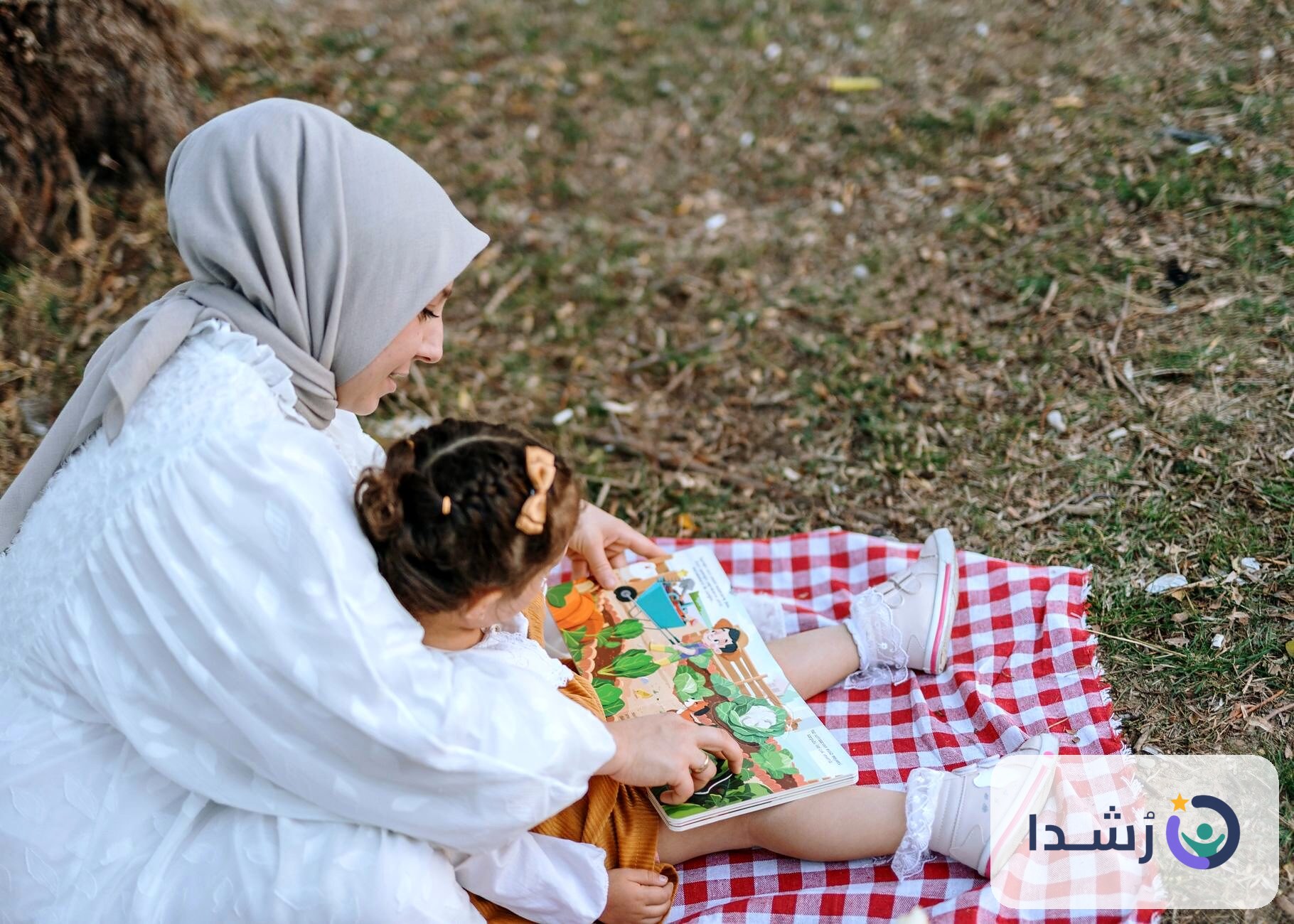 أم تقرأ لطفلتها في حديقة، مع كتاب ملون.